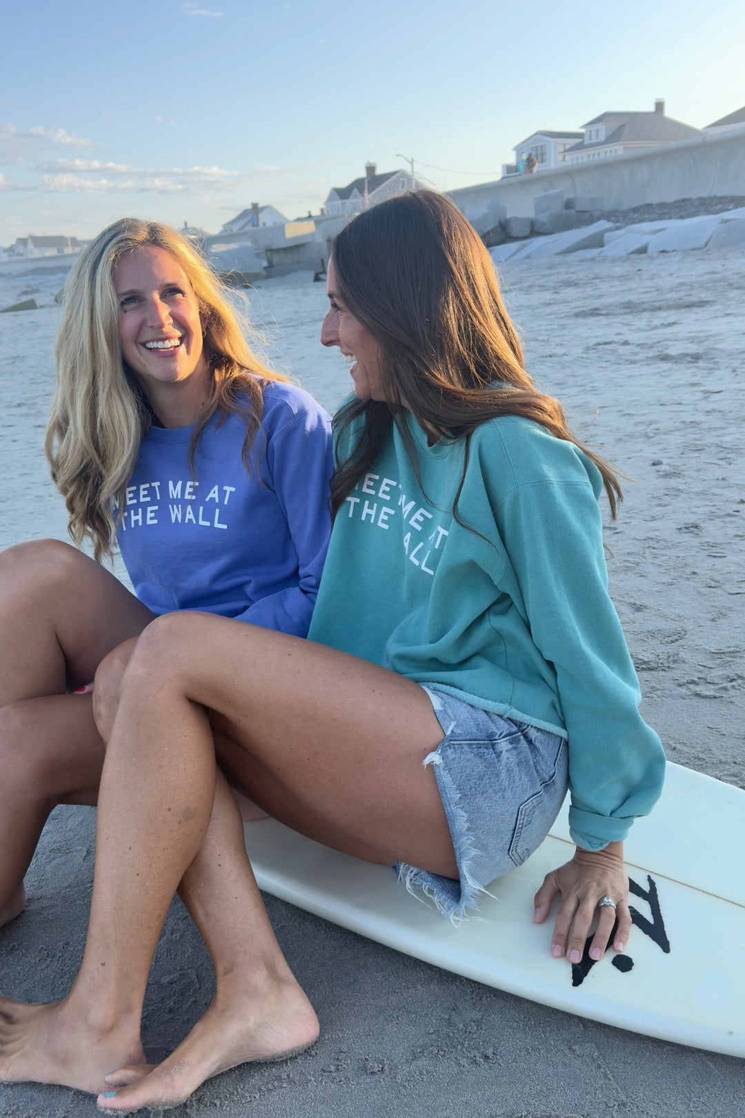 Friends in Meet Me At The Wall sweatshirts sitting on a surfboard