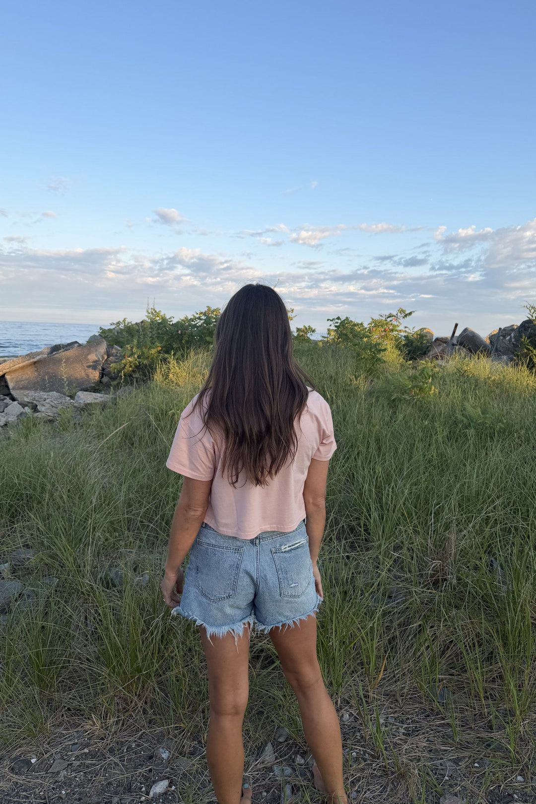 Strong Roots peach crop tee on model, back view in beach grass