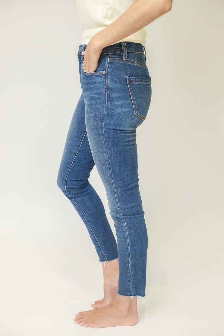 Side view of mid rise skinny jeans in medium wash with raw ankle hem