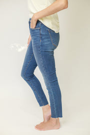 Side view of mid rise skinny jeans in medium wash with raw ankle hem
