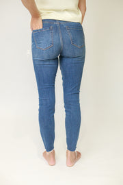 Back view of woman wearing mid rise skinny jeans in medium wash with raw ankle hem